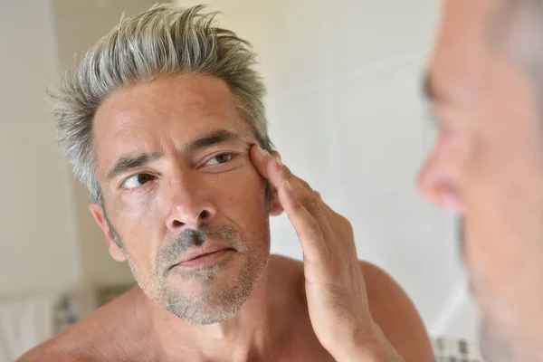 Man in front of mirror applying cream — Stock Photo, Image