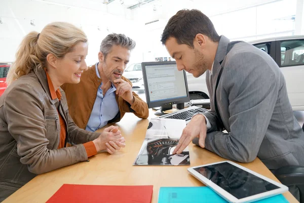 Salesman in car dealership and couple — Stock Photo, Image