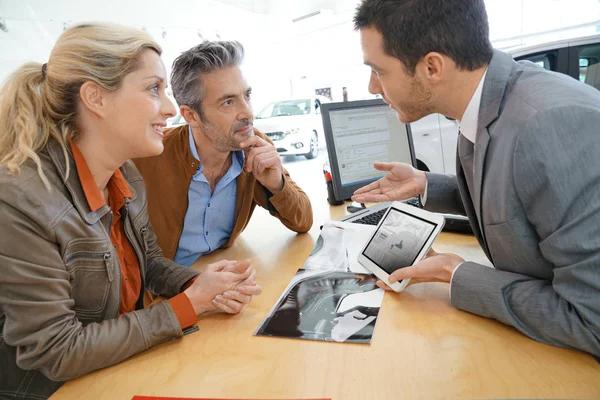 Salesman in car dealership and couple — Stock Photo, Image