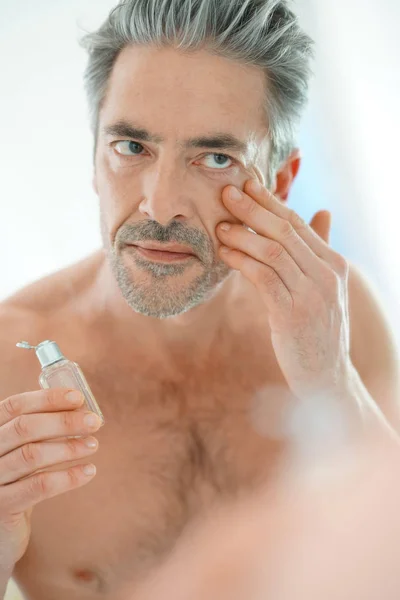 Homem maduro aplicando creme facial — Fotografia de Stock