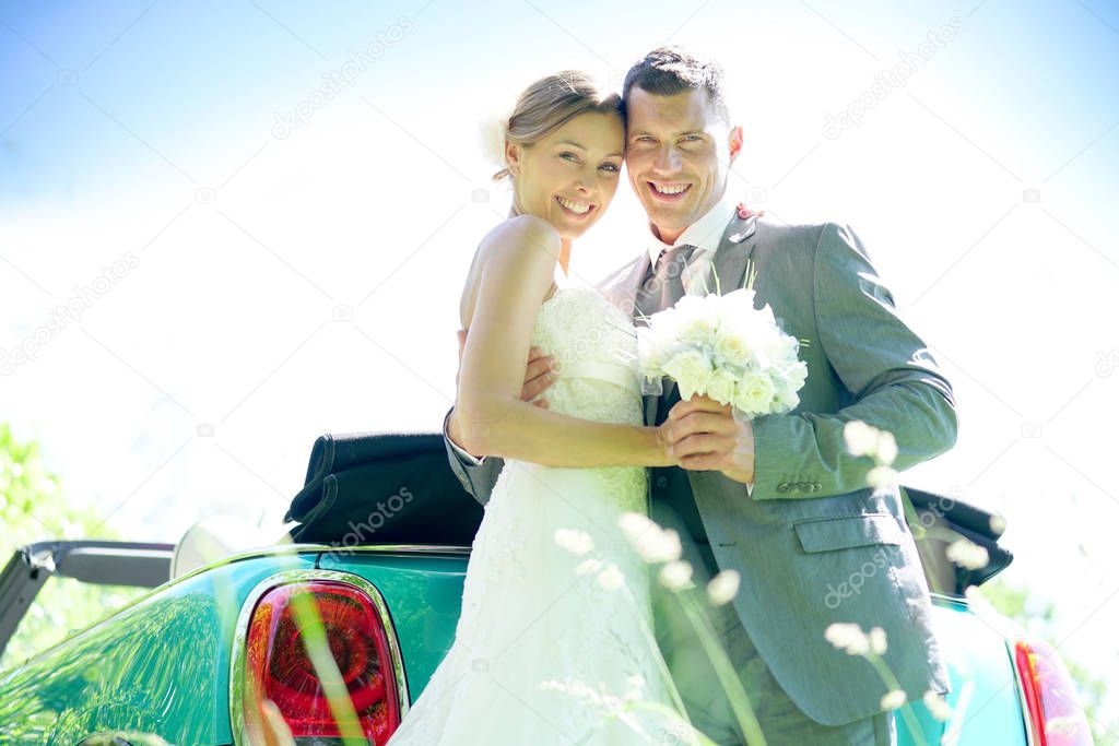 Bride and groom standing by  car 
