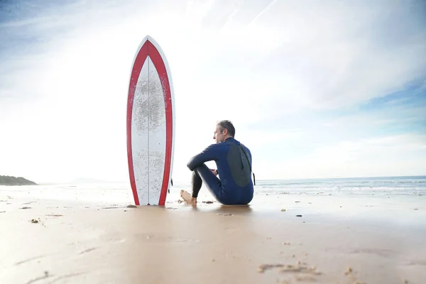 Surfer sitting on sandy beach — Stock Photo, Image