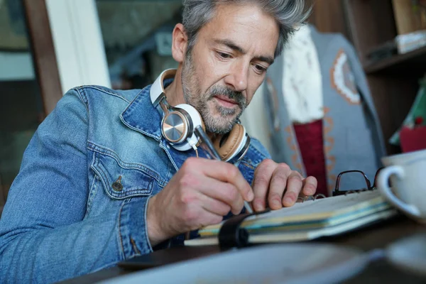 Mature man in coffee shop writing notes — Stock Photo, Image