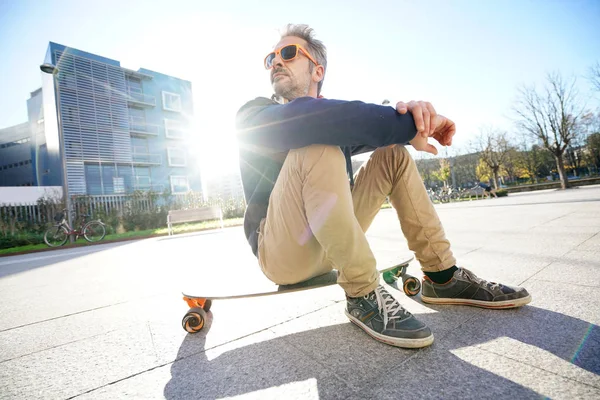 Guy sitting on skateboard in park — Stock Photo, Image