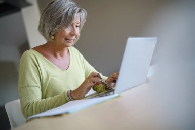 Evde kadın kıdemli dizüstü bilgisayar kullanarak