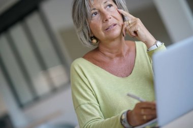 Evde kadın kıdemli dizüstü bilgisayar kullanarak