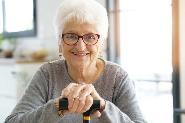 Sonriente anciana sosteniendo bastón — Foto de Stock