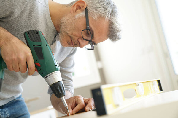 Мужчина собирает мебель с помощью электрической дрели
