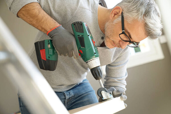 Мужчина собирает мебель с помощью электрической дрели
