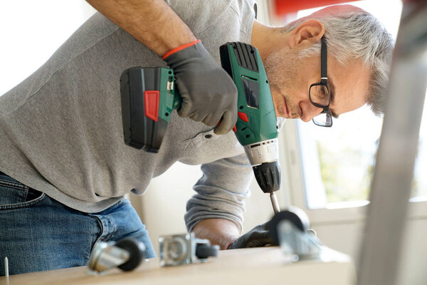 Мужчина собирает мебель с помощью электрической дрели
