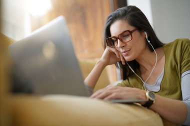 Trendy kadın evde rahatlatıcı dizüstü bilgisayar ile bağlı