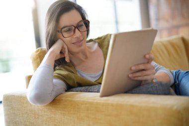 Tablet, koltukta oturan kullanma gözlük ile esmer kadın