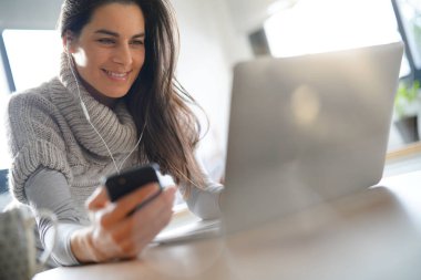 Kulaklık kullanarak dizüstü bilgisayar ve smartphone, bağlı kadın