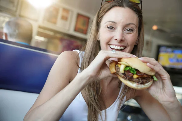 ファーストフード店でハンバーガーを食べて陽気な少女の肖像画 — ストック写真