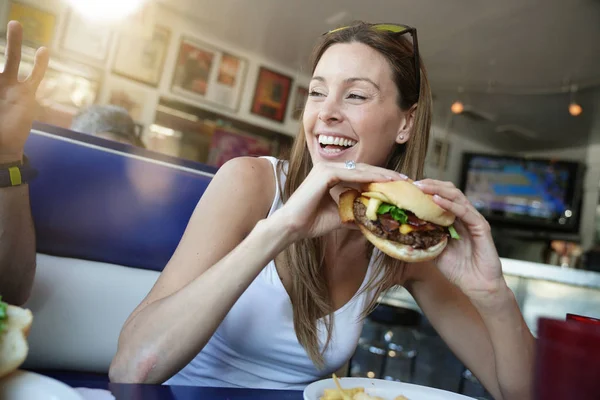 ファーストフード店でハンバーガーを食べて陽気な少女の肖像画 — ストック写真