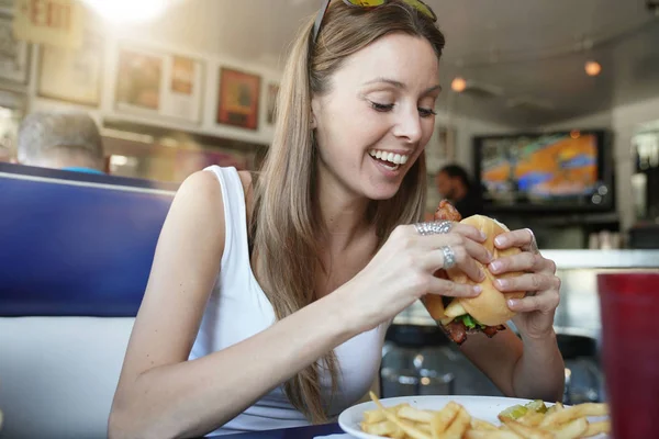 ファーストフード店でハンバーガーを食べて陽気な少女の肖像画 — ストック写真