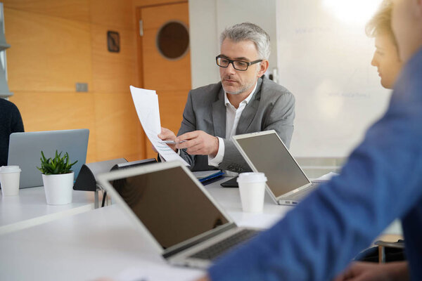 Teacher with students working around table, using laptops