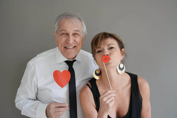 Cheerful senior couple with photobooth props, isolated