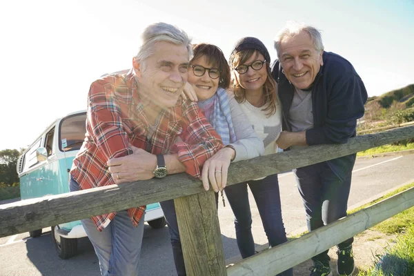 Senior friends on a road trip leaning on fence by the sea