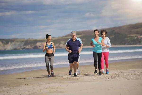 Senior people and sports coach running on sandy beach