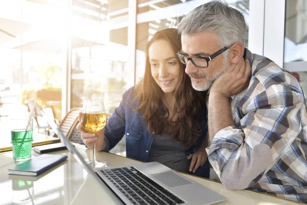 Couple in bar connected on laptop computer, having a drink