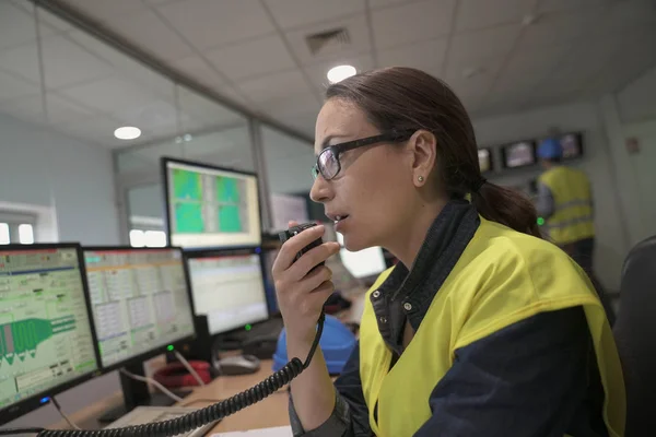Woman in industrial control room using radio to give instructions