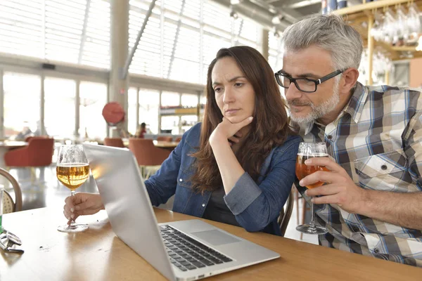 Couple in bar connected on laptop computer, having a drink