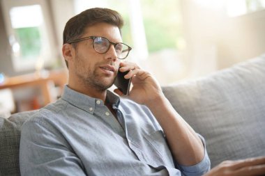 Kanepede dinlenen, telefonda konuşan gülümseyen adam.