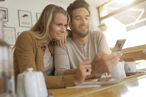 若いカップルがコーヒーショップで携帯電話を見て — ストック写真