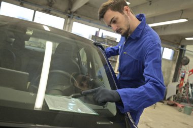 Stajyer atölyede araba motoru üzerinde çalışıyor.