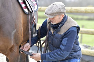 Atlı bir atı eyerliyor.