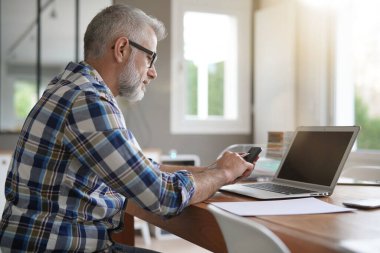 Adam evde dizüstü bilgisayar ve akıllı telefonla çalışıyor.