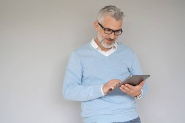 Tablet kullanan orta yaşlı bir adam, gri arka planda izole edilmiş.