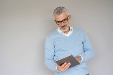 Tablet kullanan orta yaşlı bir adam, gri arka planda izole edilmiş.