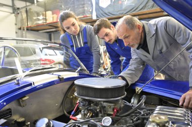 Araba motoru üzerinde çalışan stajyerleri olan bir eğitmen. 