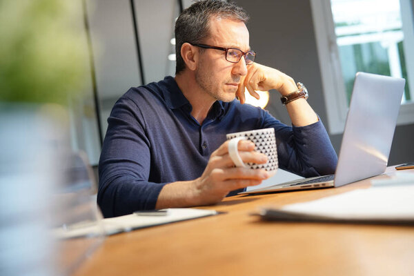 Middle-aged guy having hot drink, working on laptop