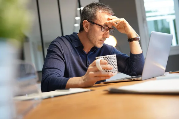 Middle-aged guy having hot drink, working on laptop