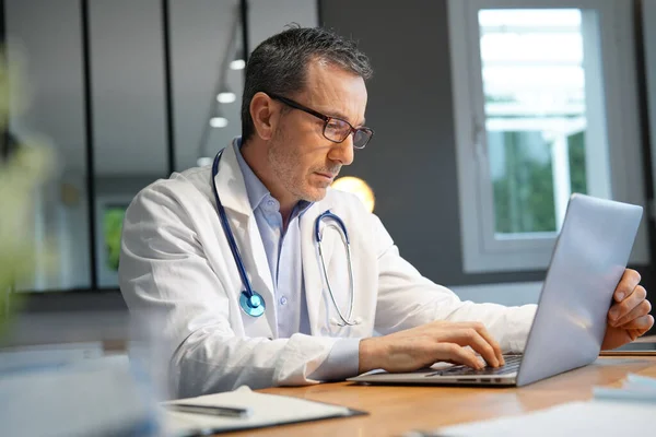 Doctor in office working on laptop