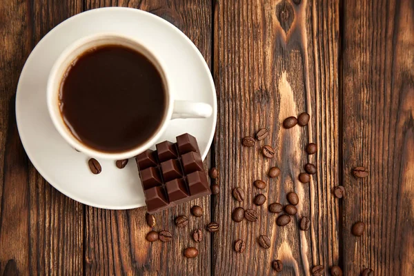 Café expreso y chocolate con granos de café dispersos en la vieja mesa oscura de madera — Foto de Stock