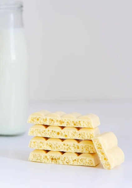 Uma garrafa de leite e uma pirâmide de chocolate poroso branco em um fundo branco — Fotografia de Stock