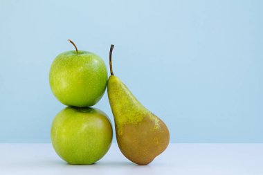 iki taze yeşil elma ve mavi arka plan üzerinde bir uzun armut