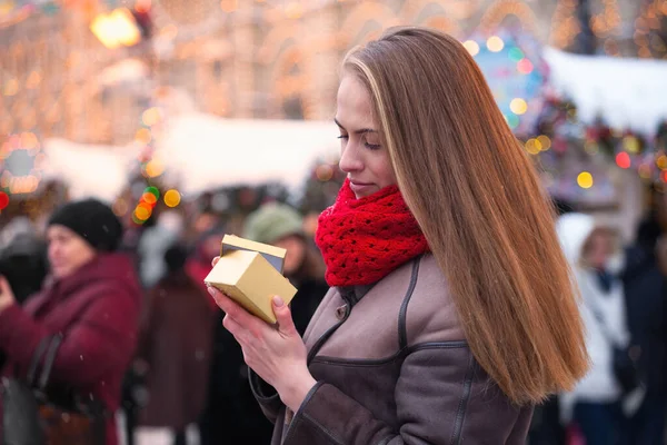 Mujer joven abre un regalo en un mercado de Navidad. Es hora de dar regalos. El concepto de compras de Navidad y regalos de Navidad — Foto de Stock