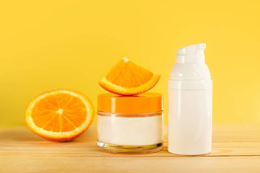 Cildin için karmaşık bir bakım. Enerji vitamini ve doğal vitaminler. Ahşap bir masa ve sarı arka planda portakallı kozmetik seti