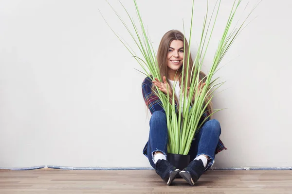 Mujer joven sosteniendo gran planta verde sentada contra la pared . —  Fotos de Stock