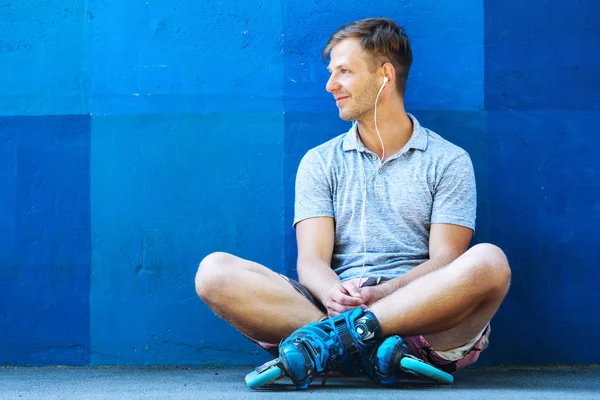 Feliz bonito jovem rolo em patins em linha sentado contra blu — Fotografia de Stock