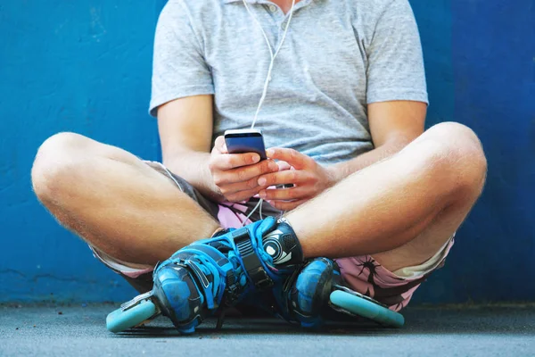 青い壁に座って携帯電話でインライン ローラー スケート. — ストック写真