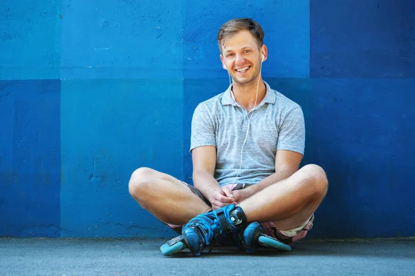 Feliz bonito jovem rolo em patins em linha sentado contra blu — Fotografia de Stock