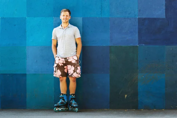 Happy handsome young roller in inline skates sitting against blu — Stock Photo, Image