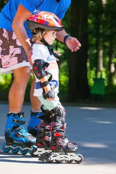 Lindo bebé con instructor de patinaje en línea en el parque —  Fotos de Stock