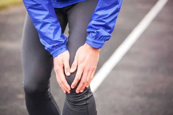 Tiro cortado de um jovem corredor segurando seu joelho ferido enquanto ru — Fotografia de Stock